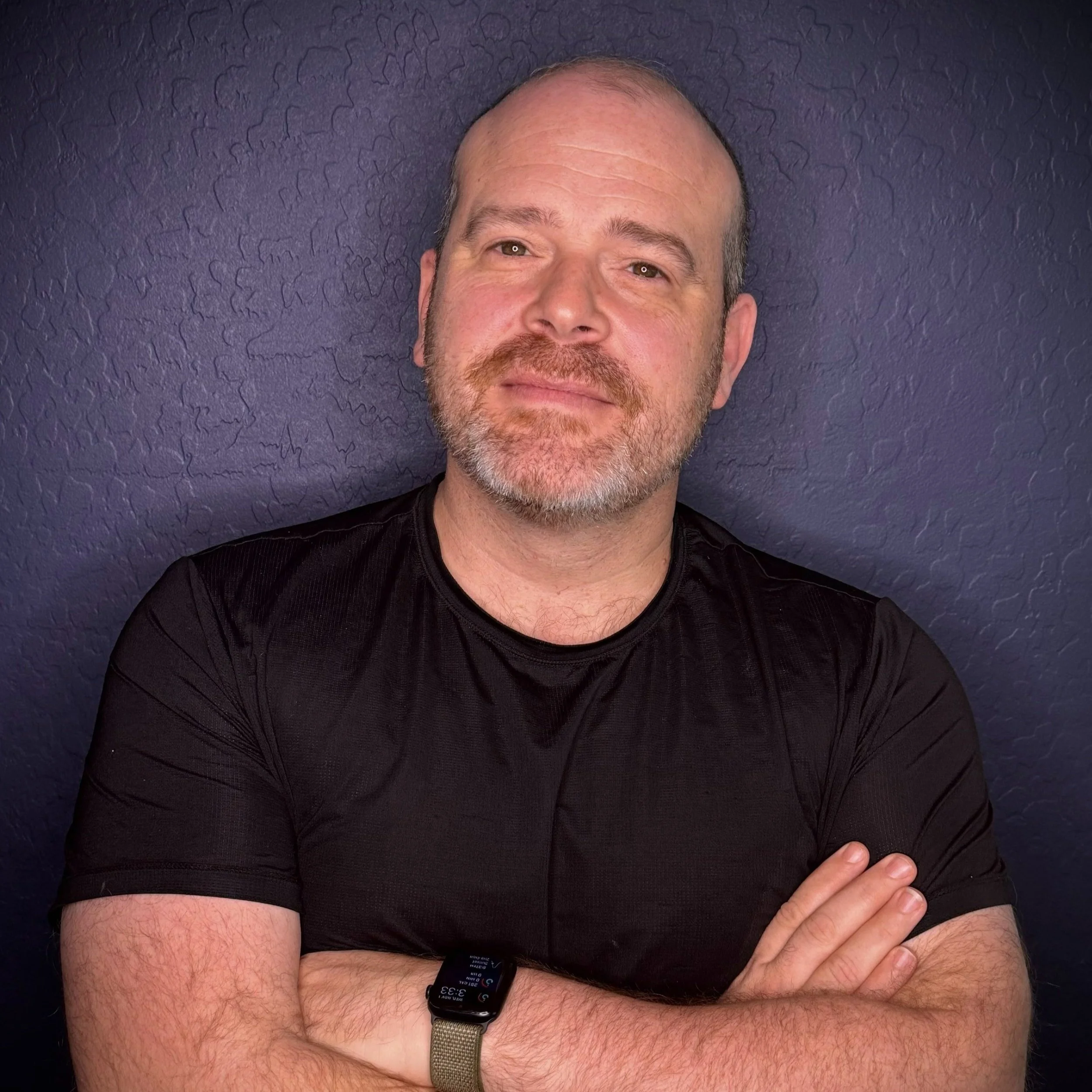 Joel B. Feldman, founder of Look Newly, smiling with arms crossed against a deep blue textured wall