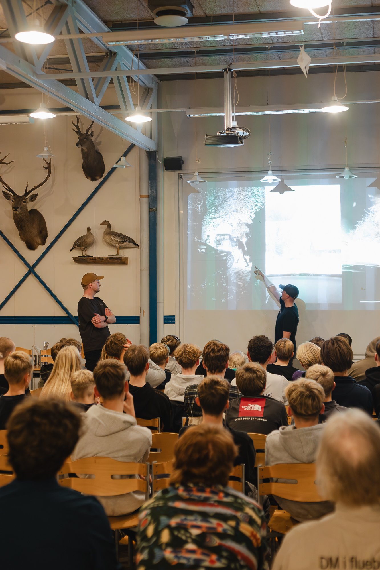 En masse unge sidder i rækker og ser en Frank Sjøgren stå foran en projektionsskærm og holder foredrag.