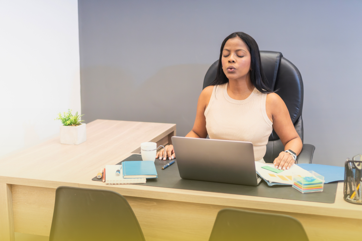 A woman takes a breath at her desk with her laptop
