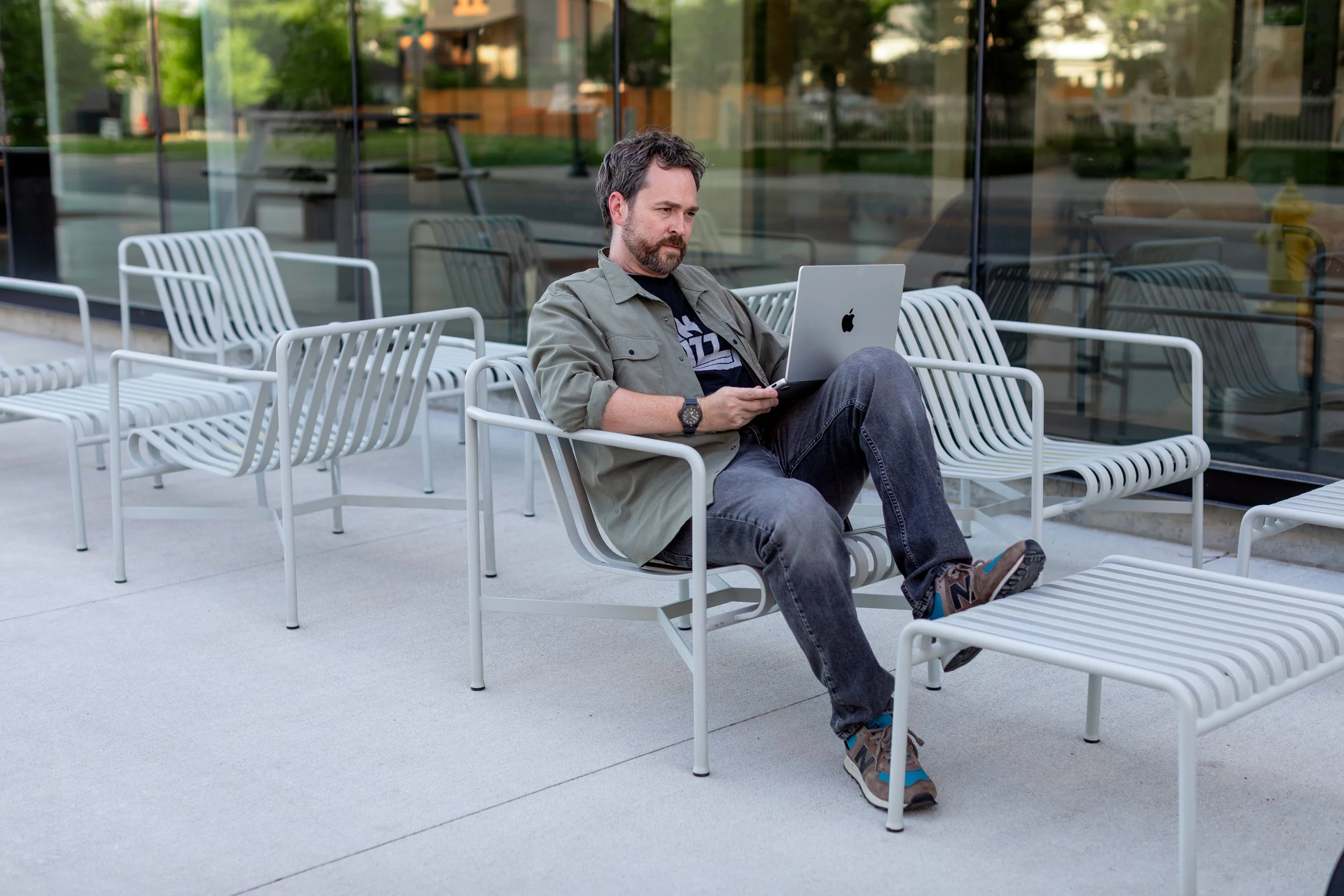 Jon Stephen-Stansel sits on an outdoor bench with his laptop.