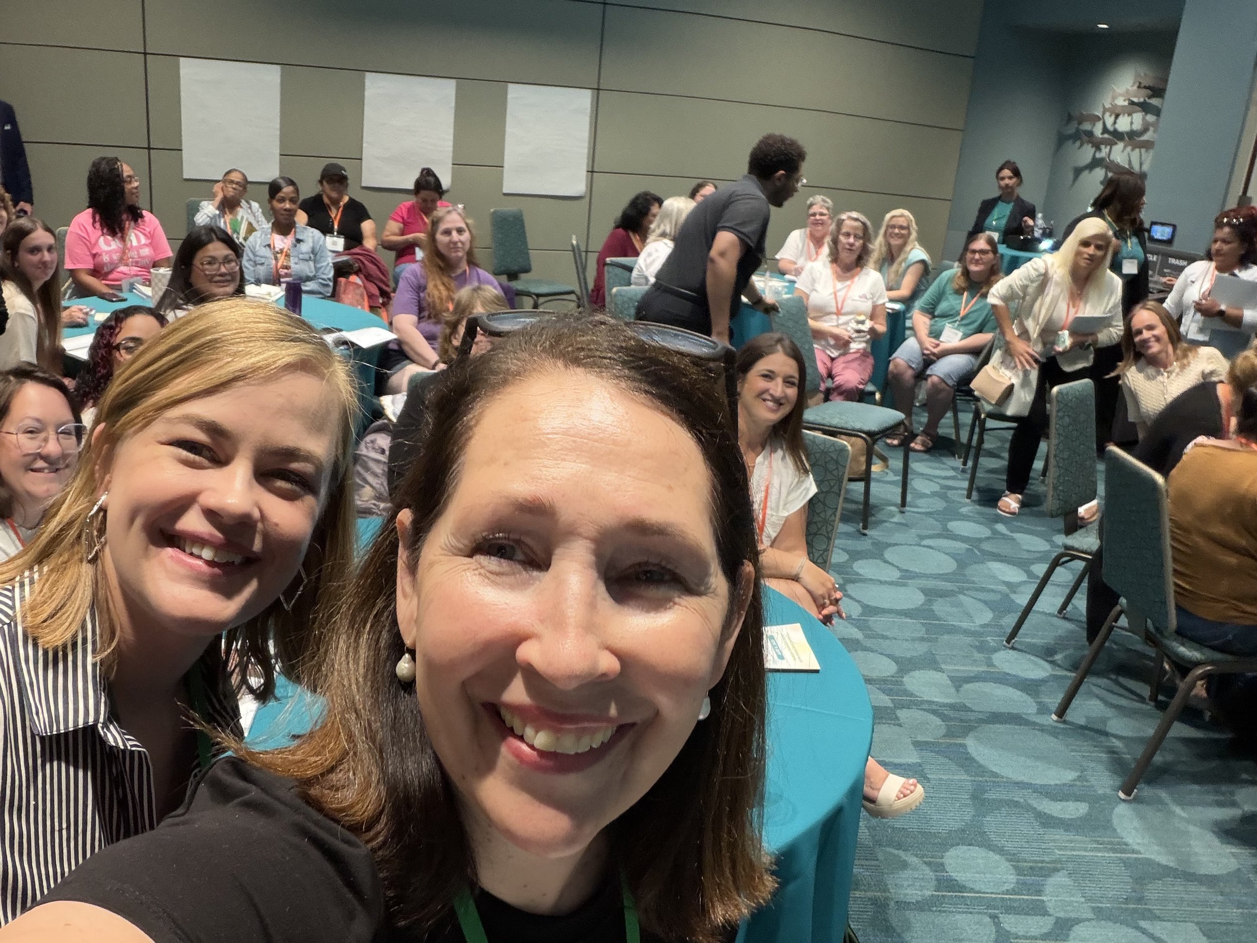 Erin Owen and Kelly Jefferson Minty take a selfie in a room where they are giving a presentation