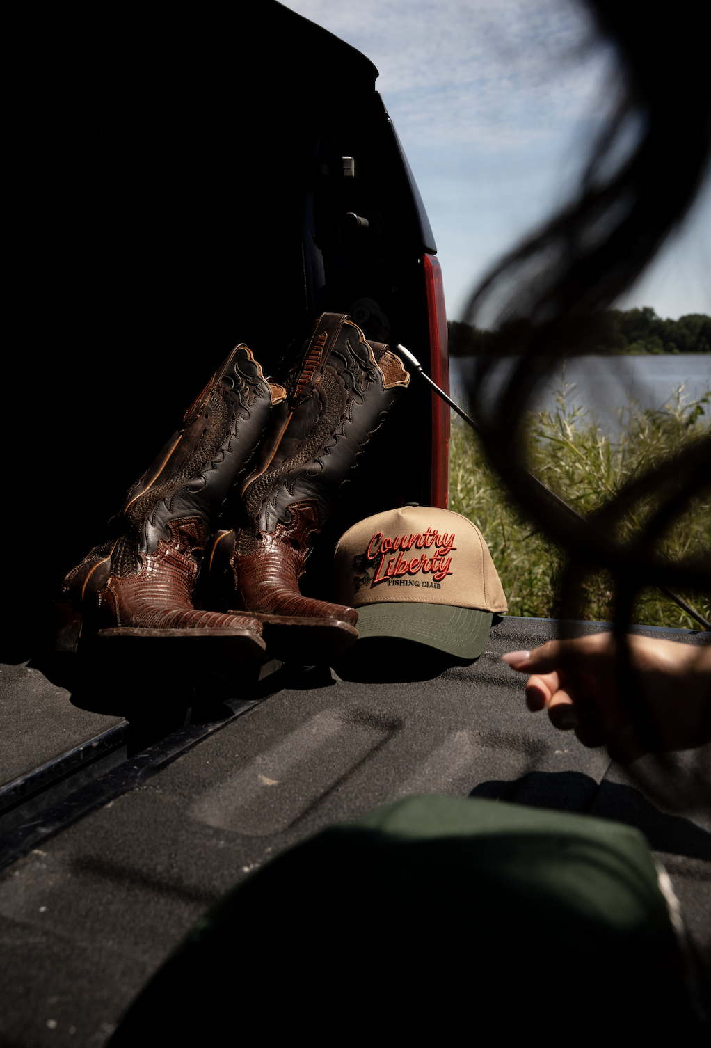Pair of worn brown boots resting on a vehicle tailgate near a grassy landscape.