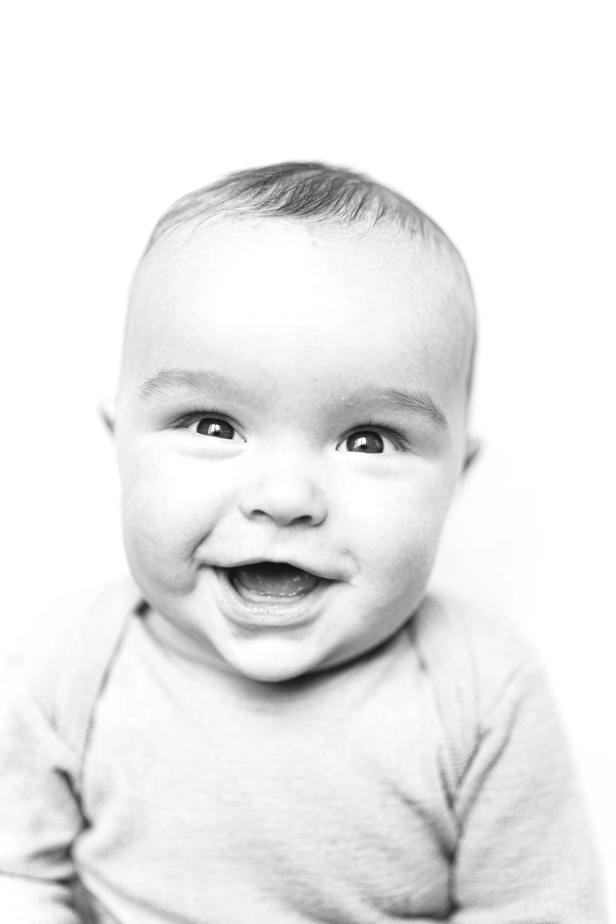 Black and white photo of a smiling baby with short hair, wearing a light-colored shirt. black and white portrait. 