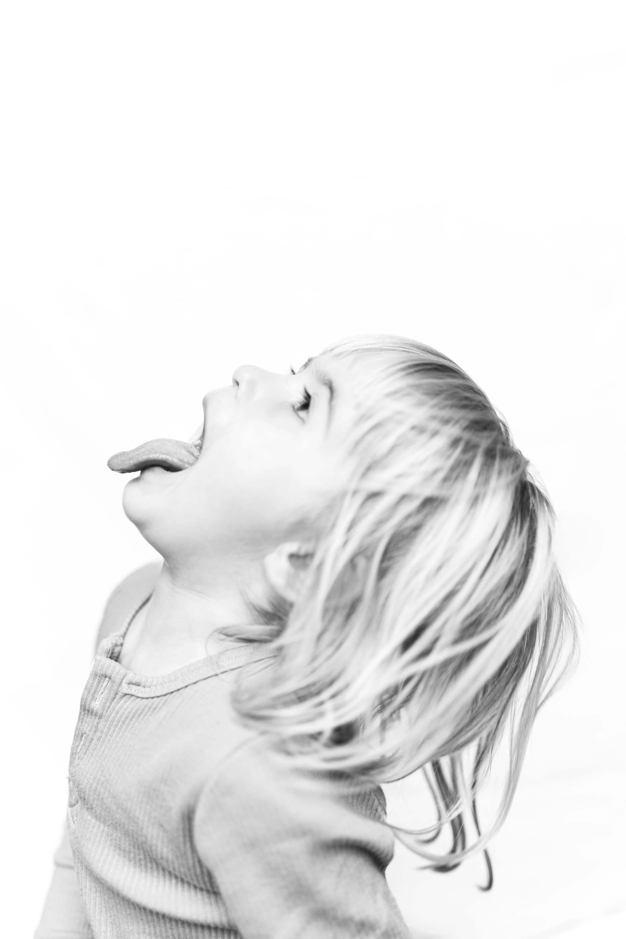 A young child with wet hair sticking out to one side, sticking out their tongue with their head tilted back. black and white portrait. 