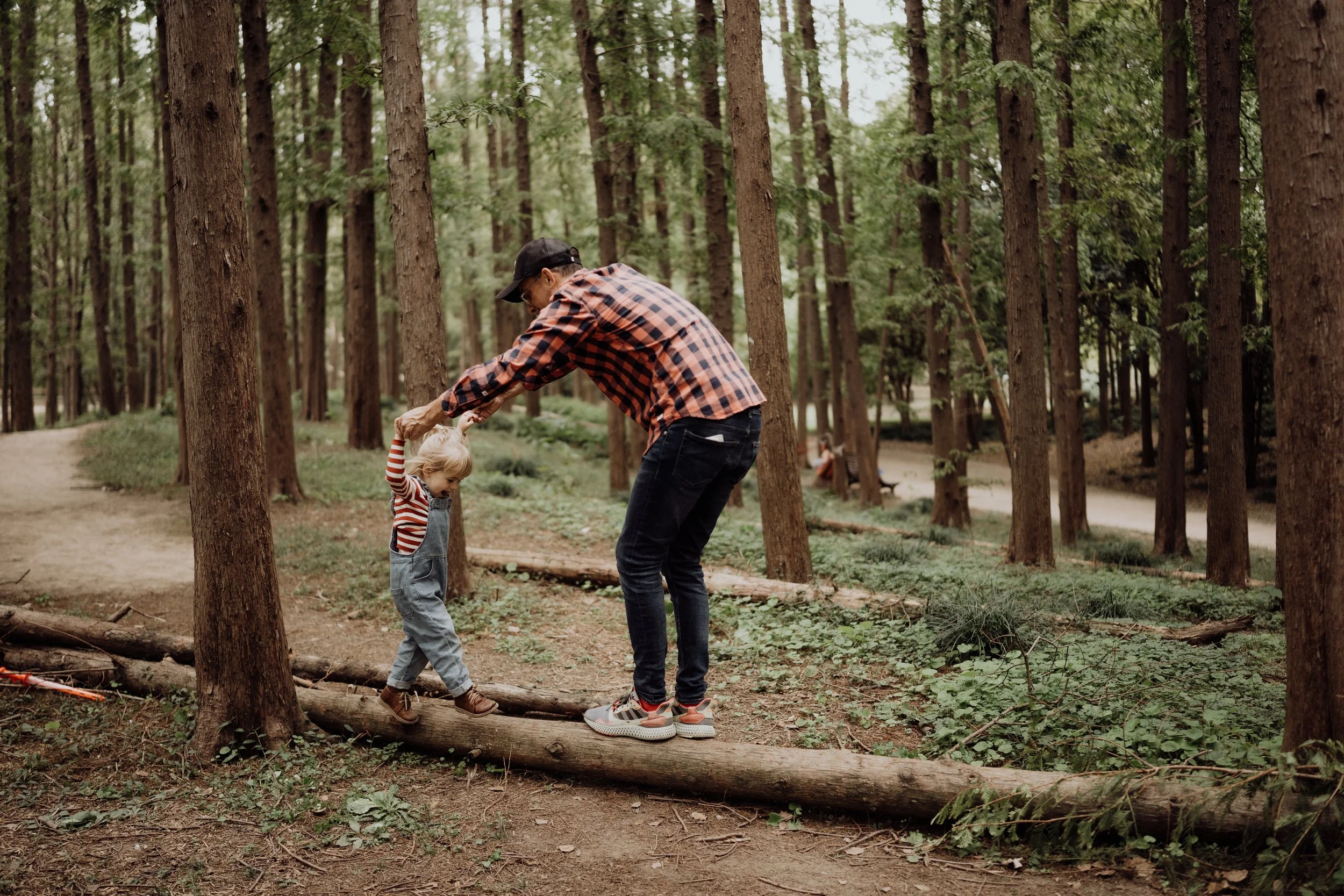 A man helping a young girl walk across a fallen log in a wooded forest