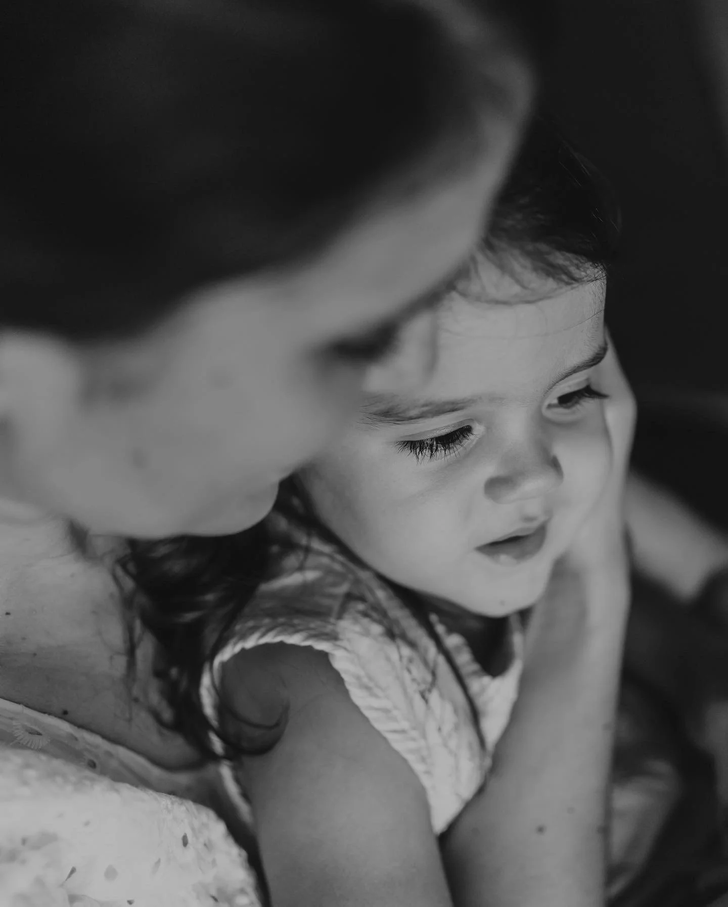 A woman and a young girl in a close, affectionate moment, both looking down and smiling gently.