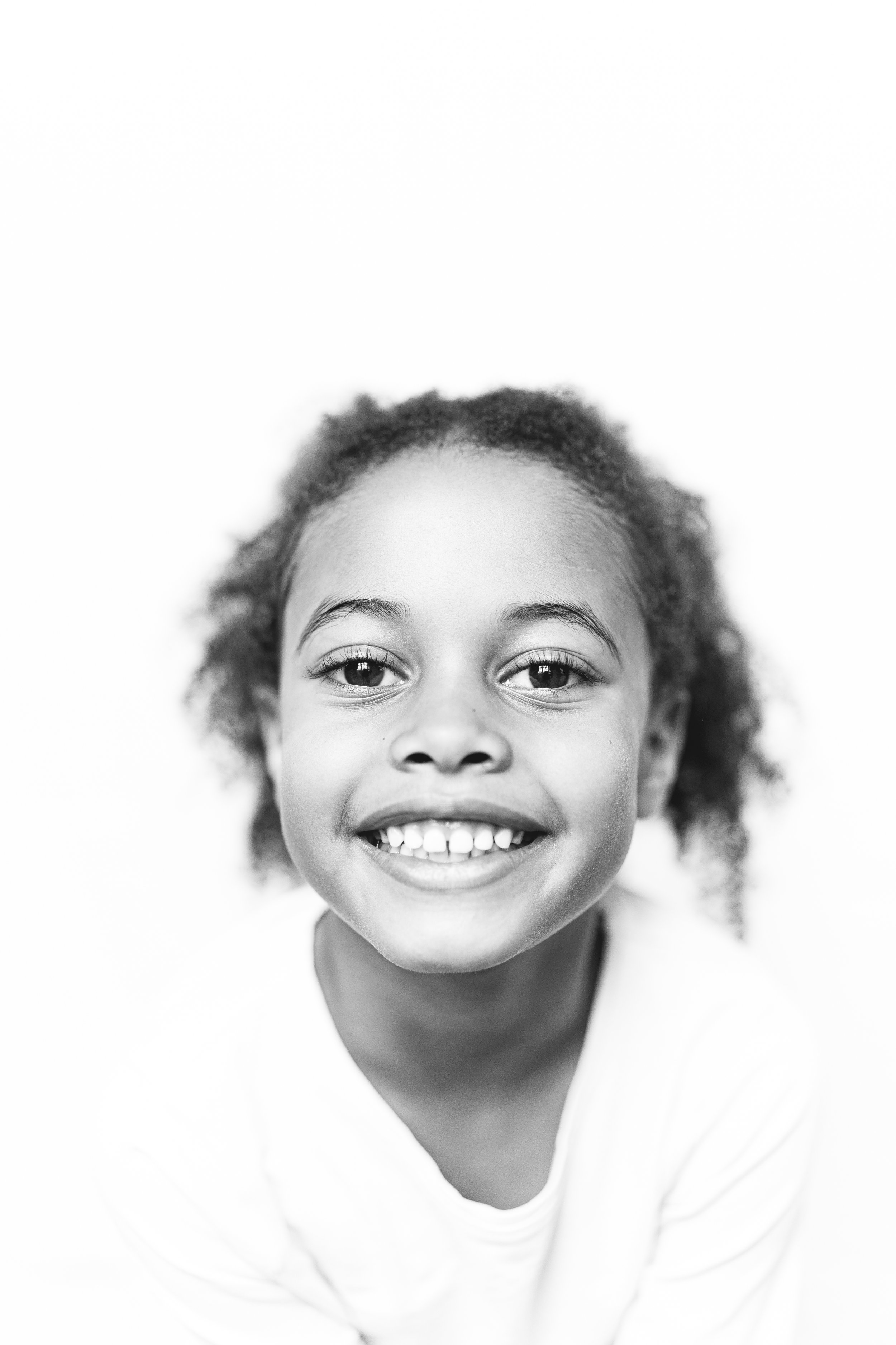 A smiling young girl with curly hair in a black and white portrait.