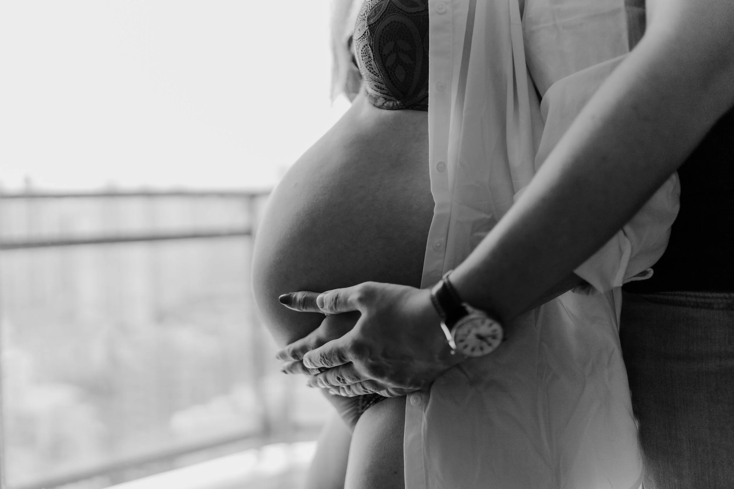 Close-up black and white photo of a pregnant woman's belly being gently held by a man's hands.