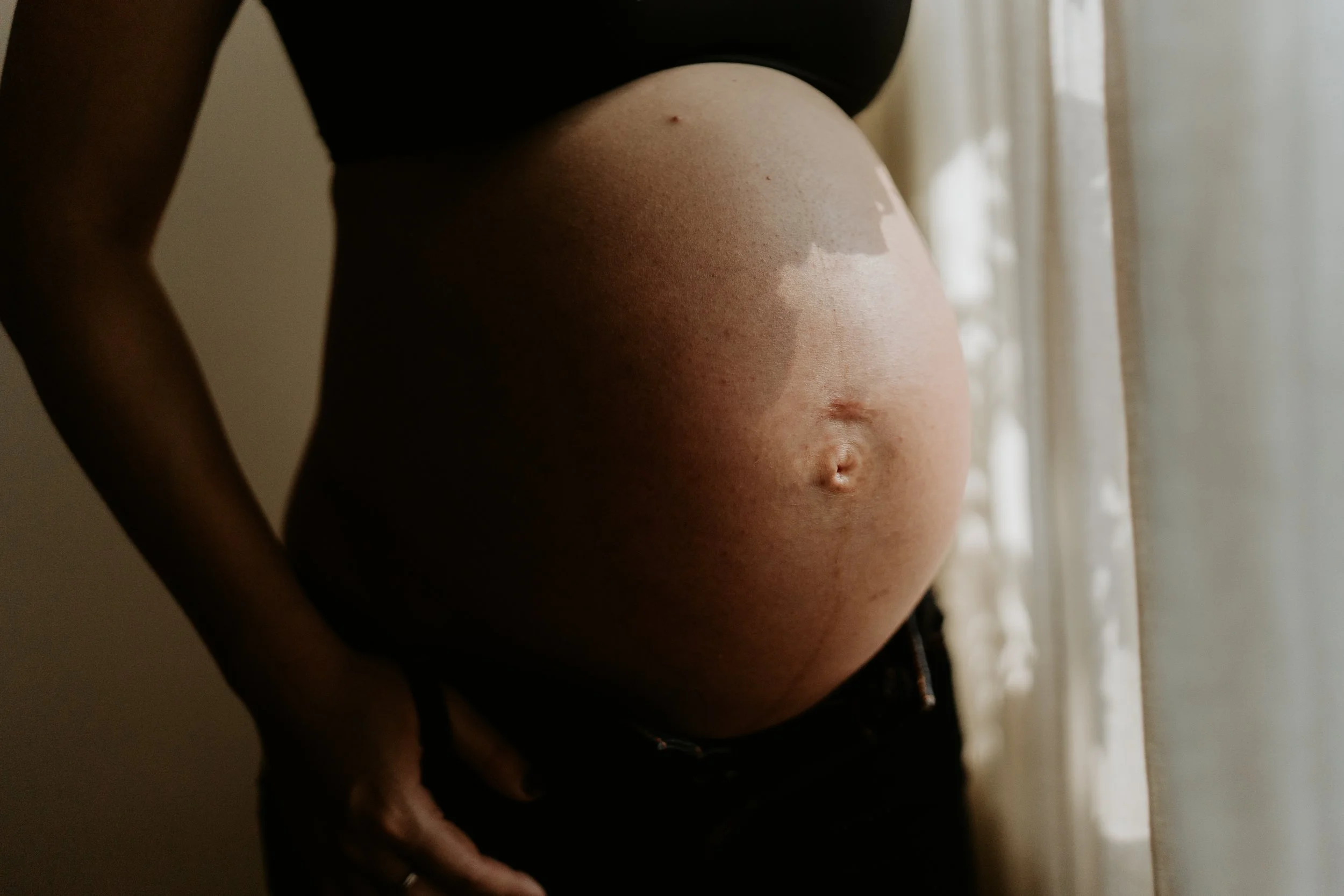 Close-up of a pregnant woman's belly near a window with sunlight streaming in.
