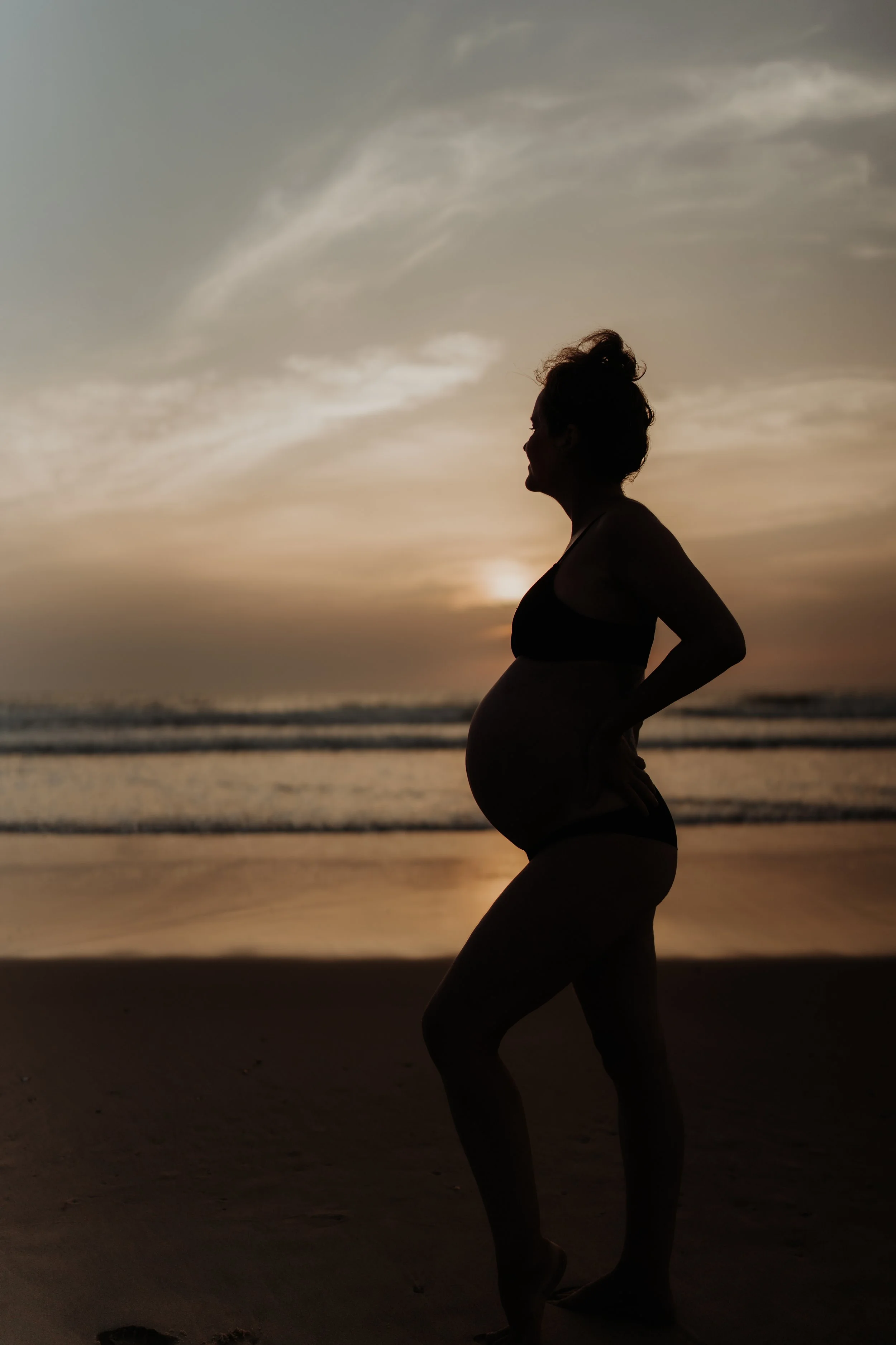 Silhouette of a pregnant woman standing on the beach during sunset.