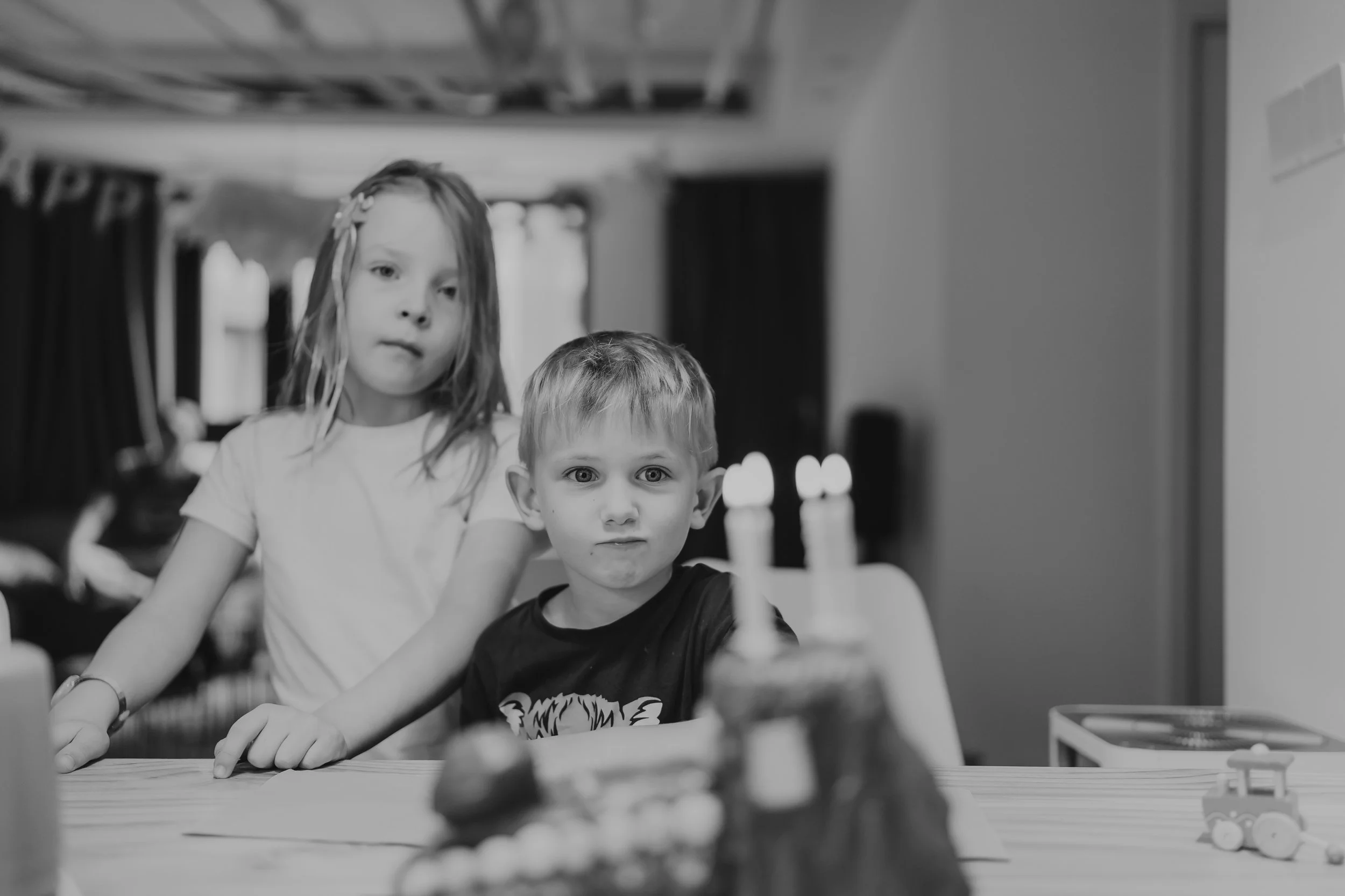 Two children, a girl and a boy, celebrate a birthday with a cake and lit candles indoors. black and white