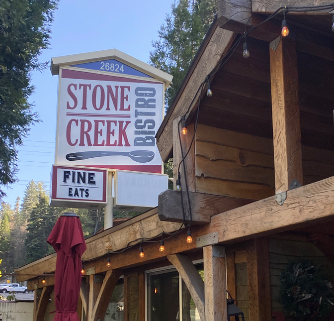 Sign for Stone Creek Bistro with the address 26824 and additional sign reading 'Fine Eats,' next to a wooden outdoor patio with string lights.