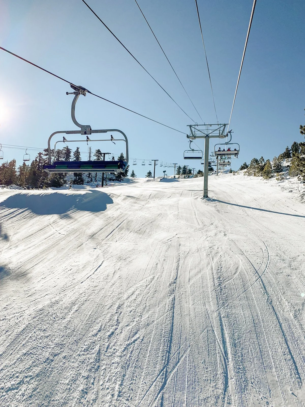 Empty ski slope with chairlifts and snow-covered trees under a clear blue sky during daytime.