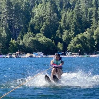 A young girl waterskiing on a lake with trees and boats in the background.