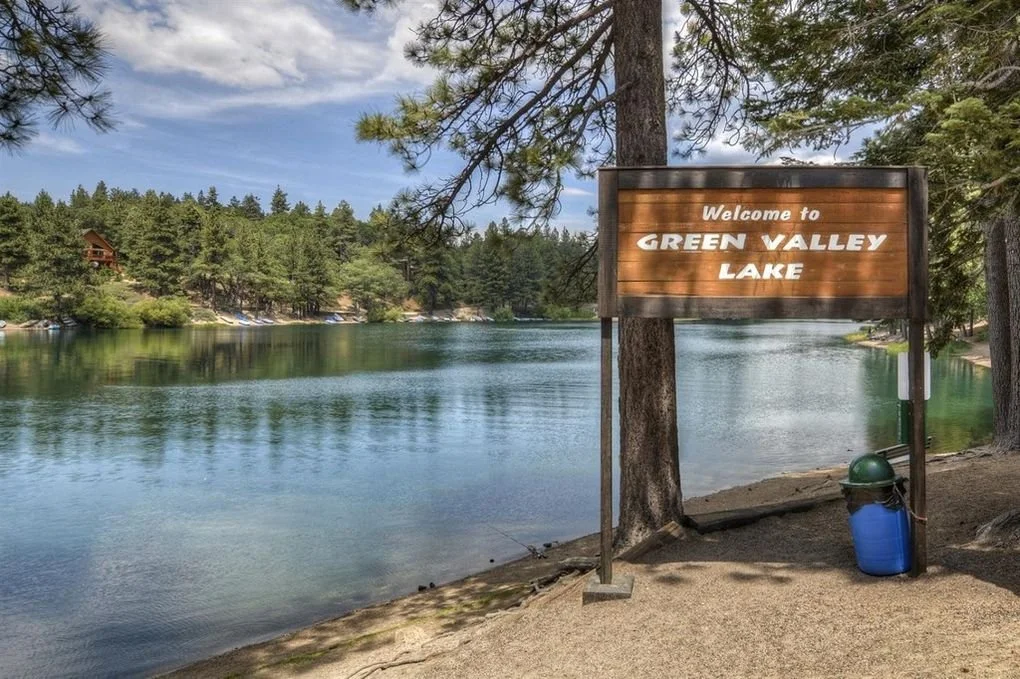 A serene mountain lake with turquoise water, surrounded by green bushes and trees under a clear blue sky.