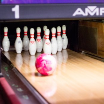 Ten bowling pins arranged in a triangle on a bowling alley with a pink marble-like bowling ball in front of them.