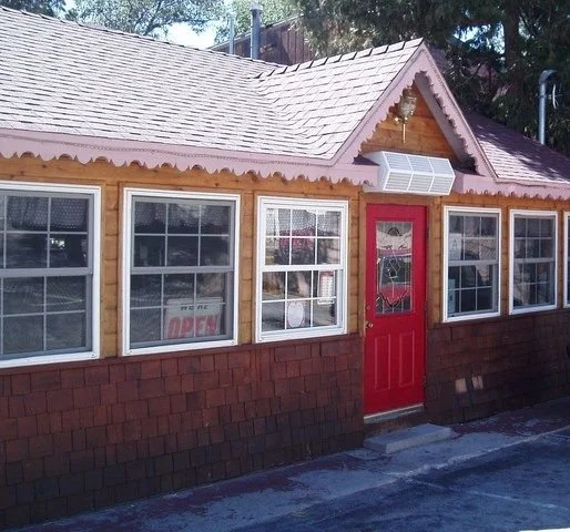 Small wooden storefront with a red door and multiple windows, one displaying an 'OPEN' sign.