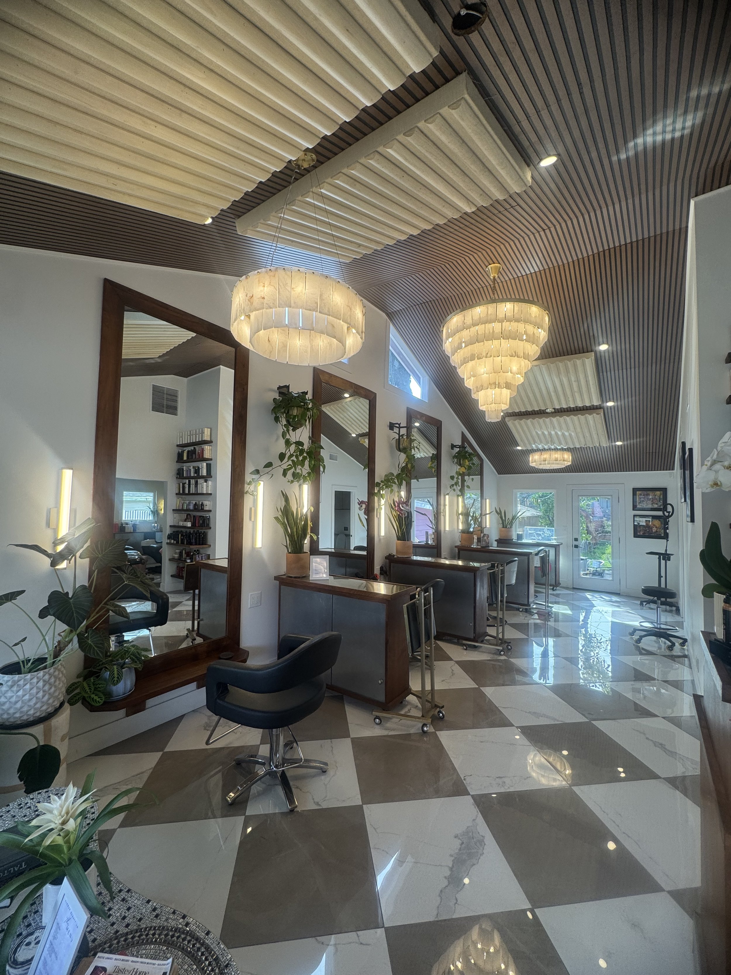 Interior of a salon with mirrors, plants, alabaster hanging chandeliers, and Edward Martin checkered floor tiles.
