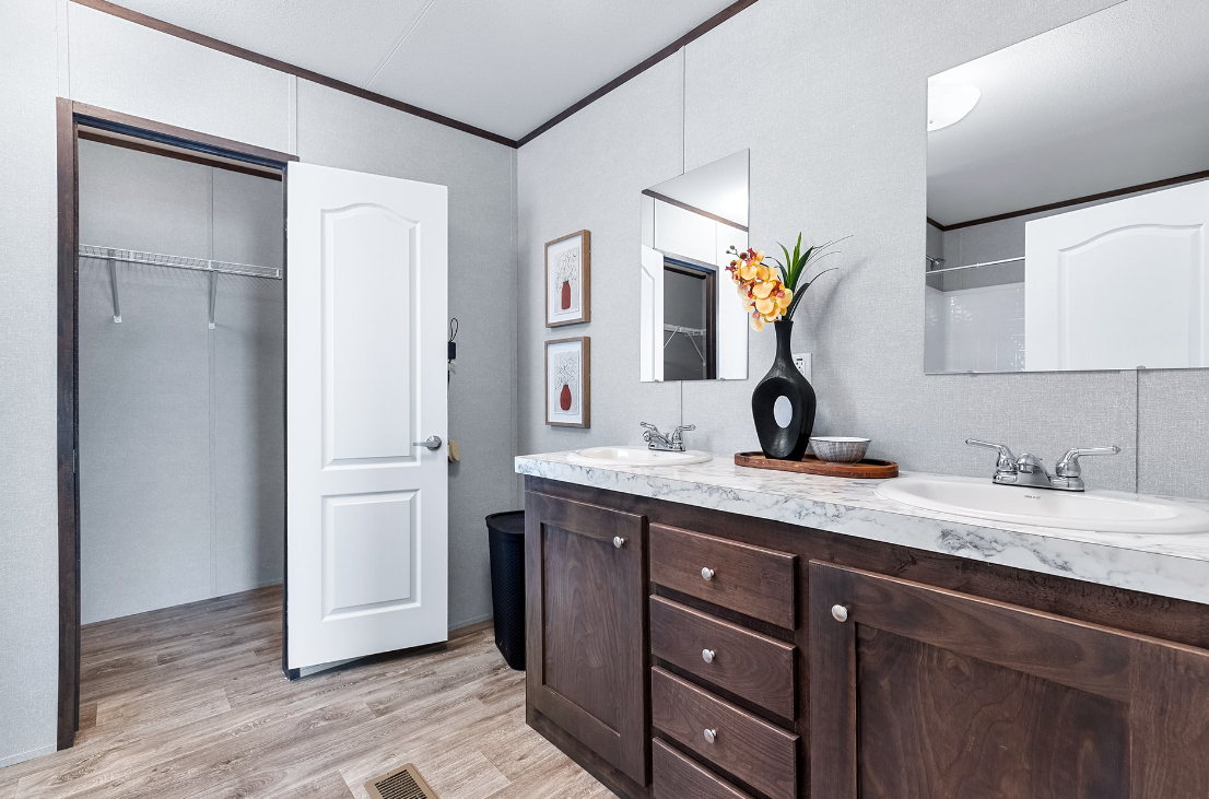 Bathroom with a double sink vanity, large mirror, decorative vase with flowers, and an open closet with a hanging rod.