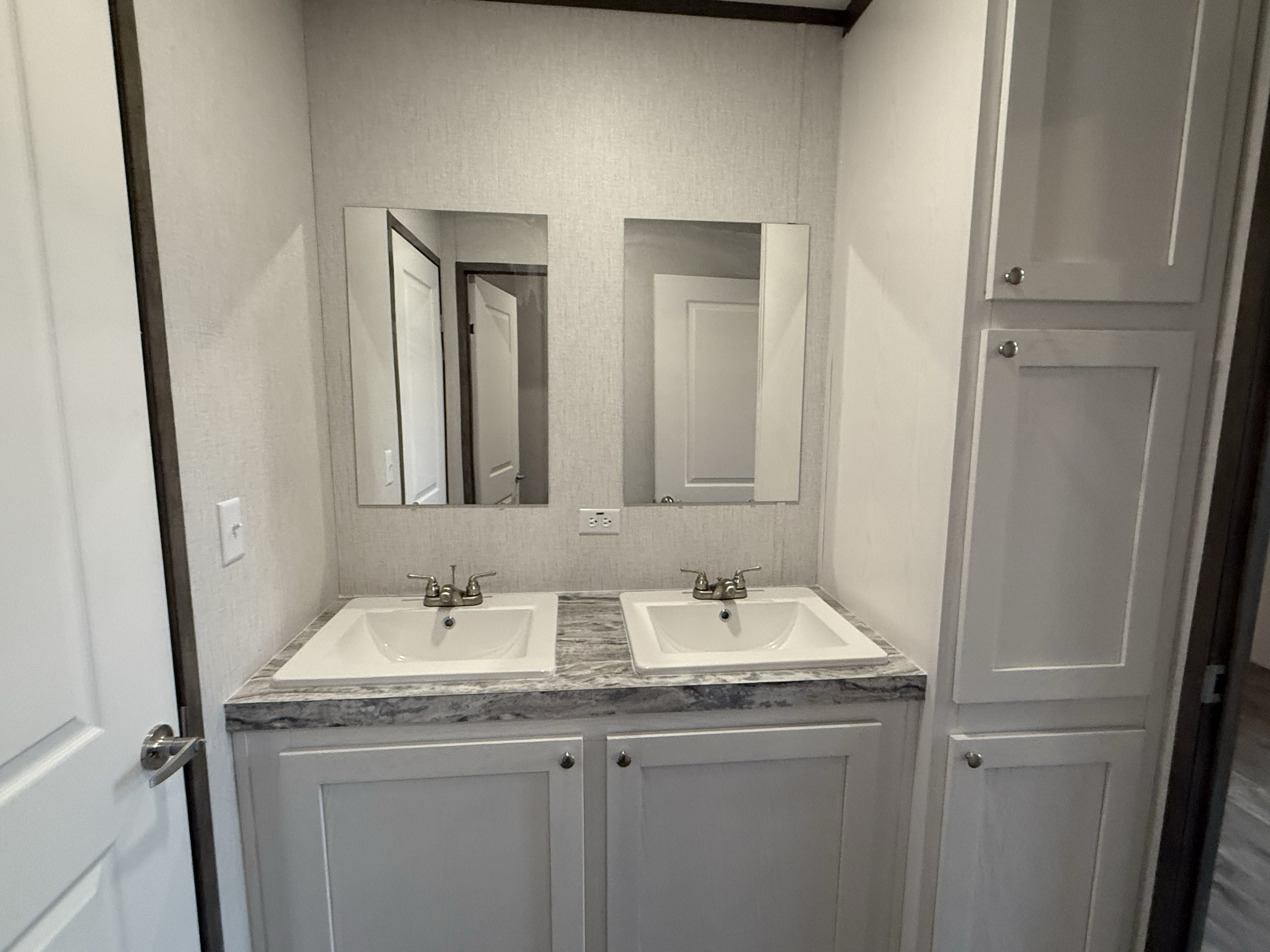 A bathroom vanity area with two white sinks, a marble countertop, two mirrors, and cabinetry on the right side.