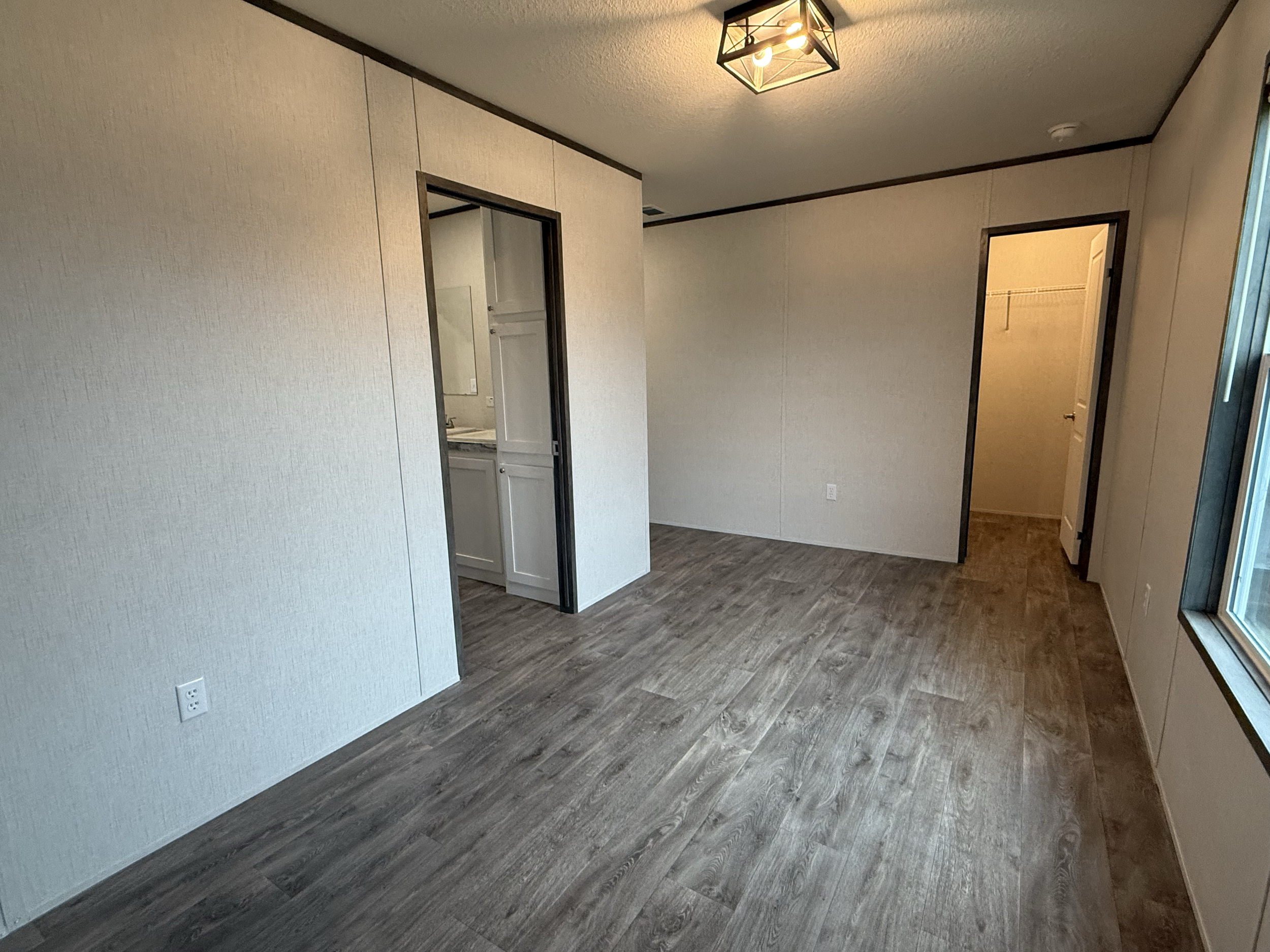 Empty room with wood flooring, beige walls, and doorways leading to a small bathroom and walk-in closet.