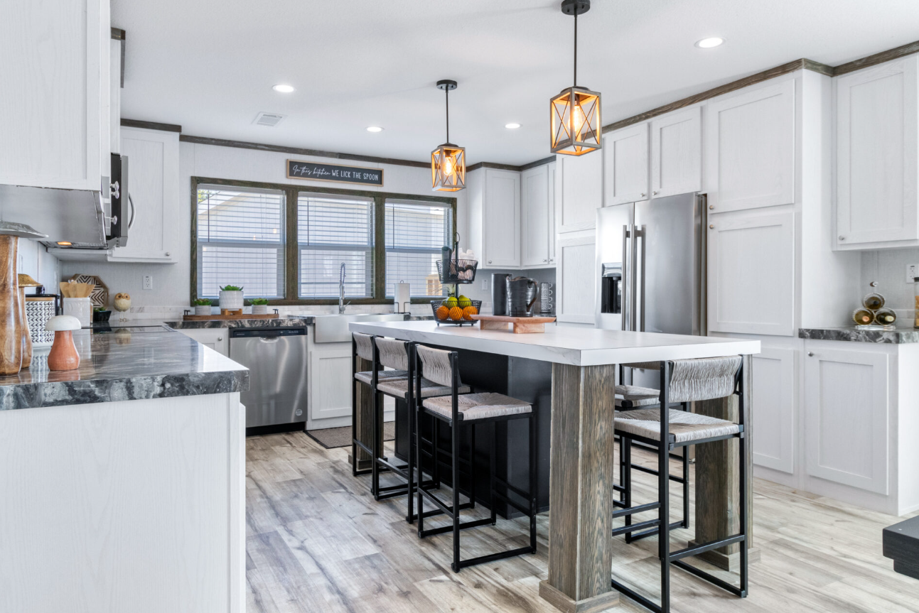 Modern kitchen with white cabinets, a kitchen island with gray and wood accents, black barstools, stainless steel appliances, and pendant lighting.