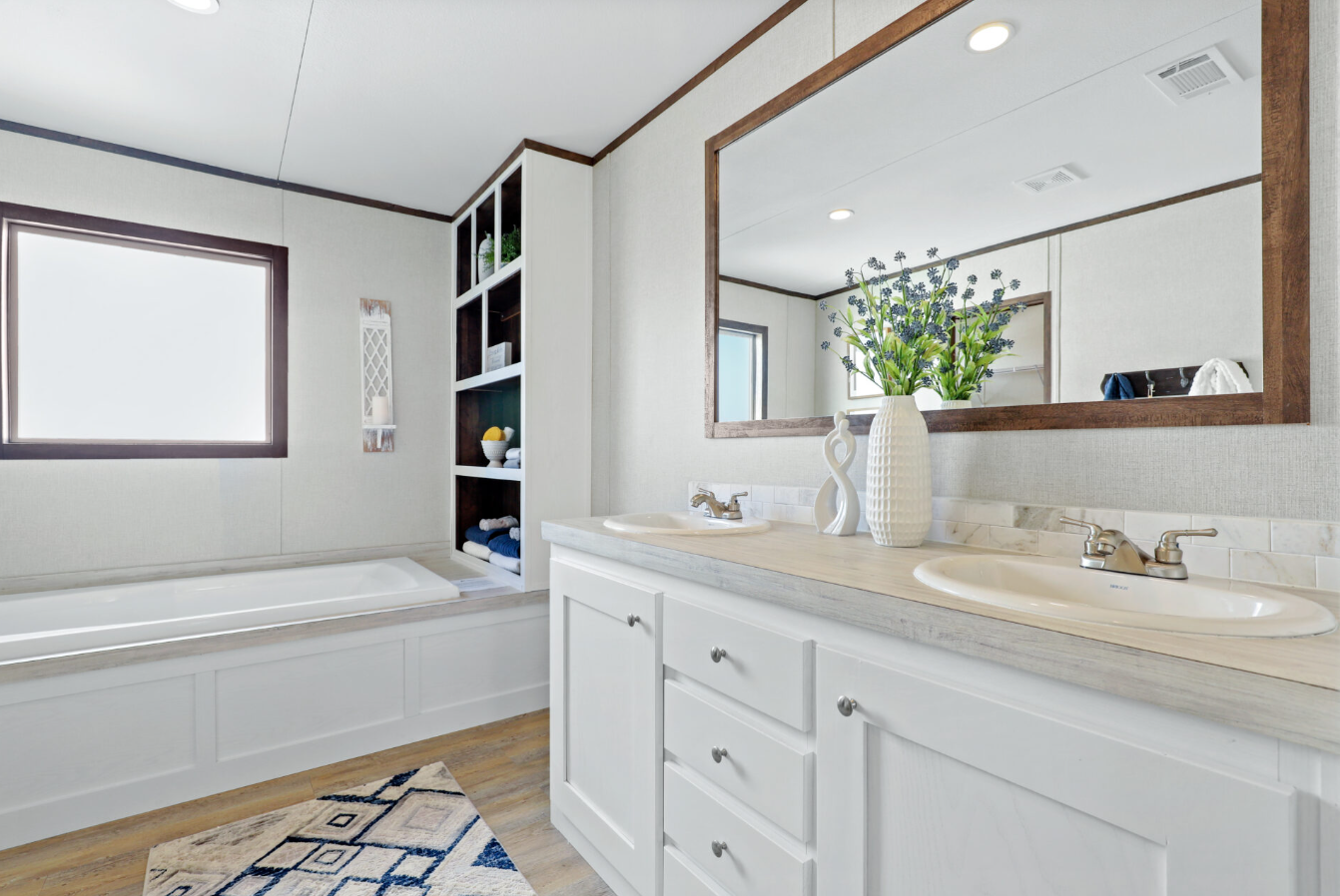 Bathroom with dual sinks, large wall mirror, built-in shelves with towels and decorative items, bathtub, window, and wooden accents.