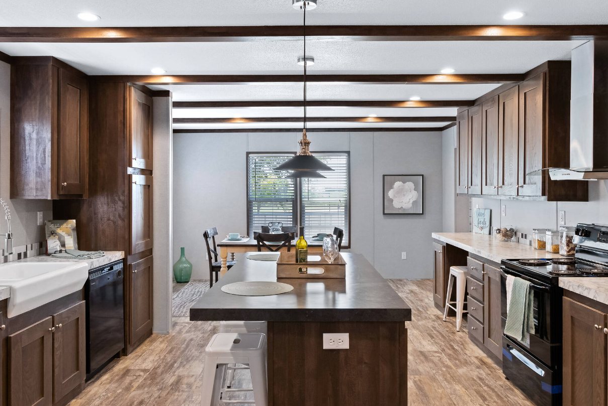 Modern kitchen with wooden cabinets, black appliances, a large island with stools, and a dining area with a table and chairs near a window.