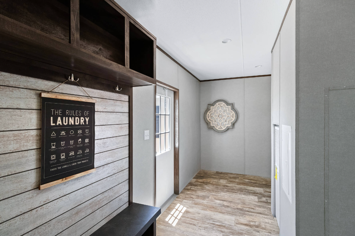 A room with wooden and light-colored wall panels, a black laundry rules sign hanging on a wooden-slatted wall, a small bench underneath, a window, and a decorative wall piece in the corner.