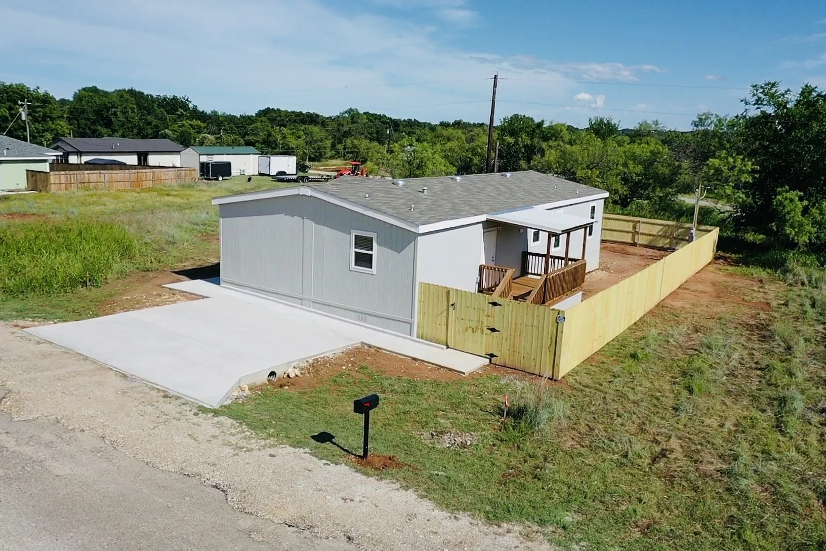 Newly built house with gray siding, a small porch with a ramp, a concrete driveway, and a wooden fence surrounding the backyard in a suburban area.