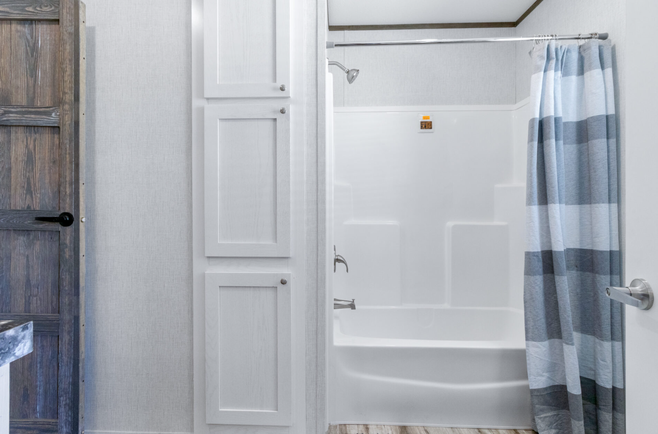 Bathroom with a white bathtub, blue and white striped shower curtain, white wall paneling, and a wooden door.