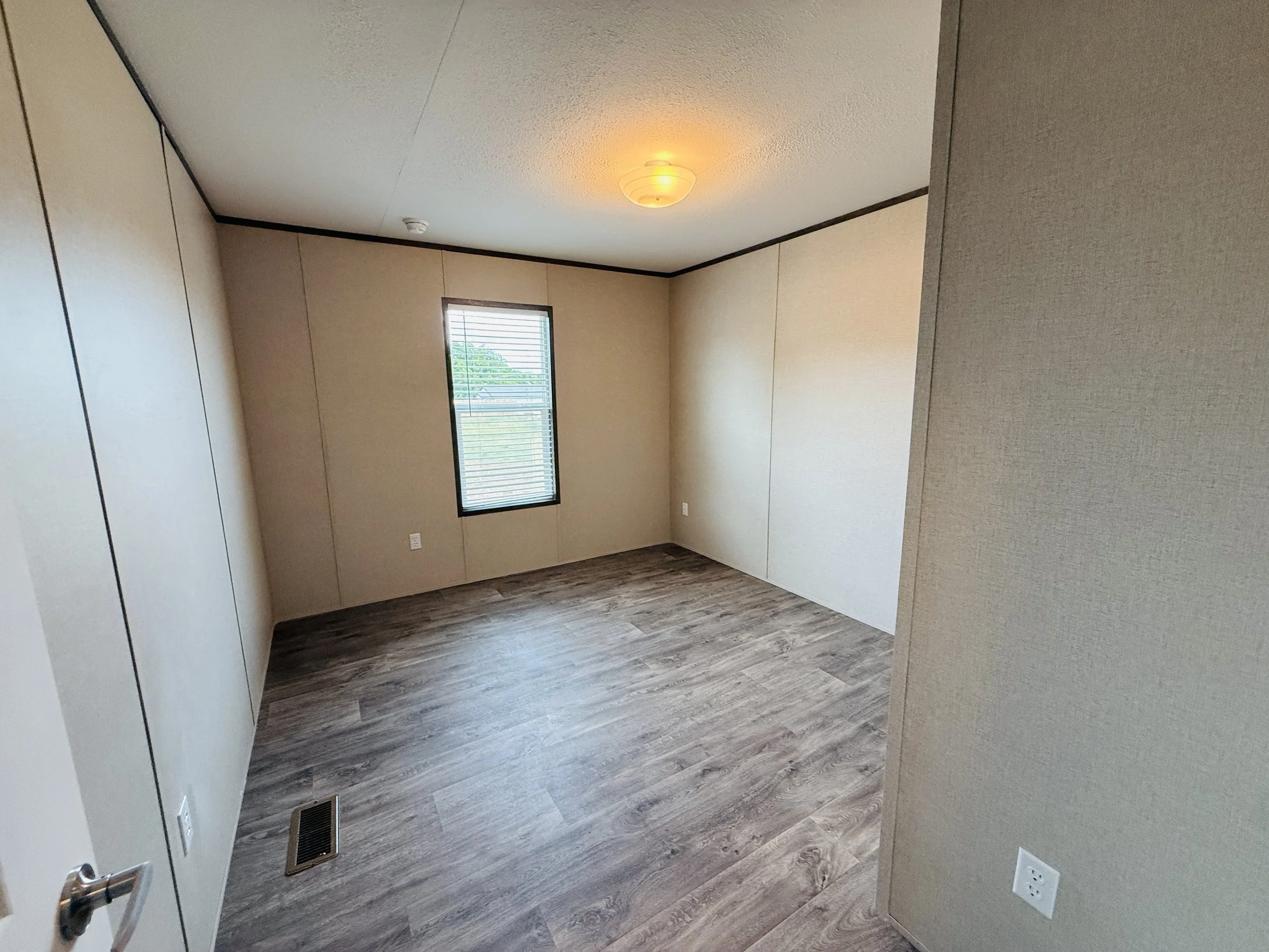 Empty room with beige walls, a window with blinds, a ceiling light, wood-look flooring, and electrical outlets.