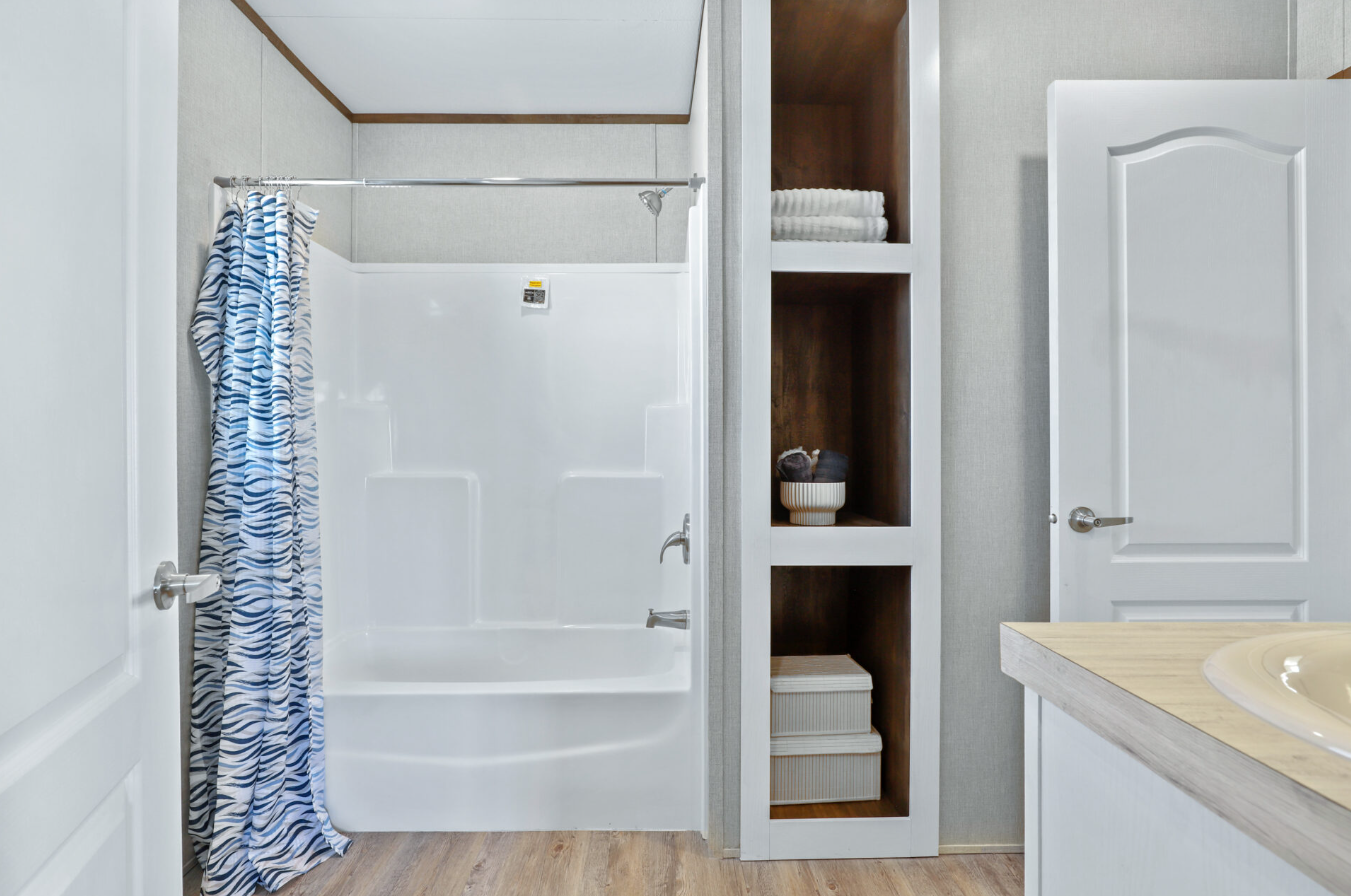 Bathroom with shower and bathtub, mirrored shower curtain with blue and white pattern, open cabinets with towels, decorative bowl, and storage boxes, and part of sink with beige countertop.