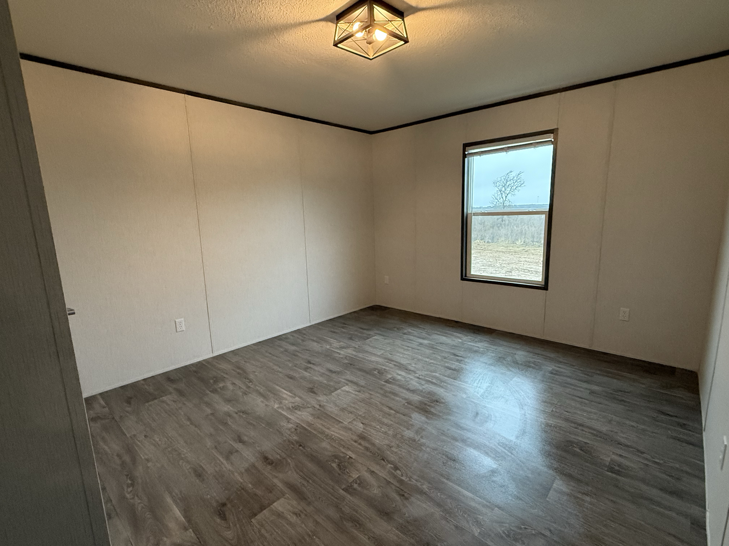 Empty room with wood-look flooring, white walls, a window showing a single tree outside, and a ceiling light fixture.