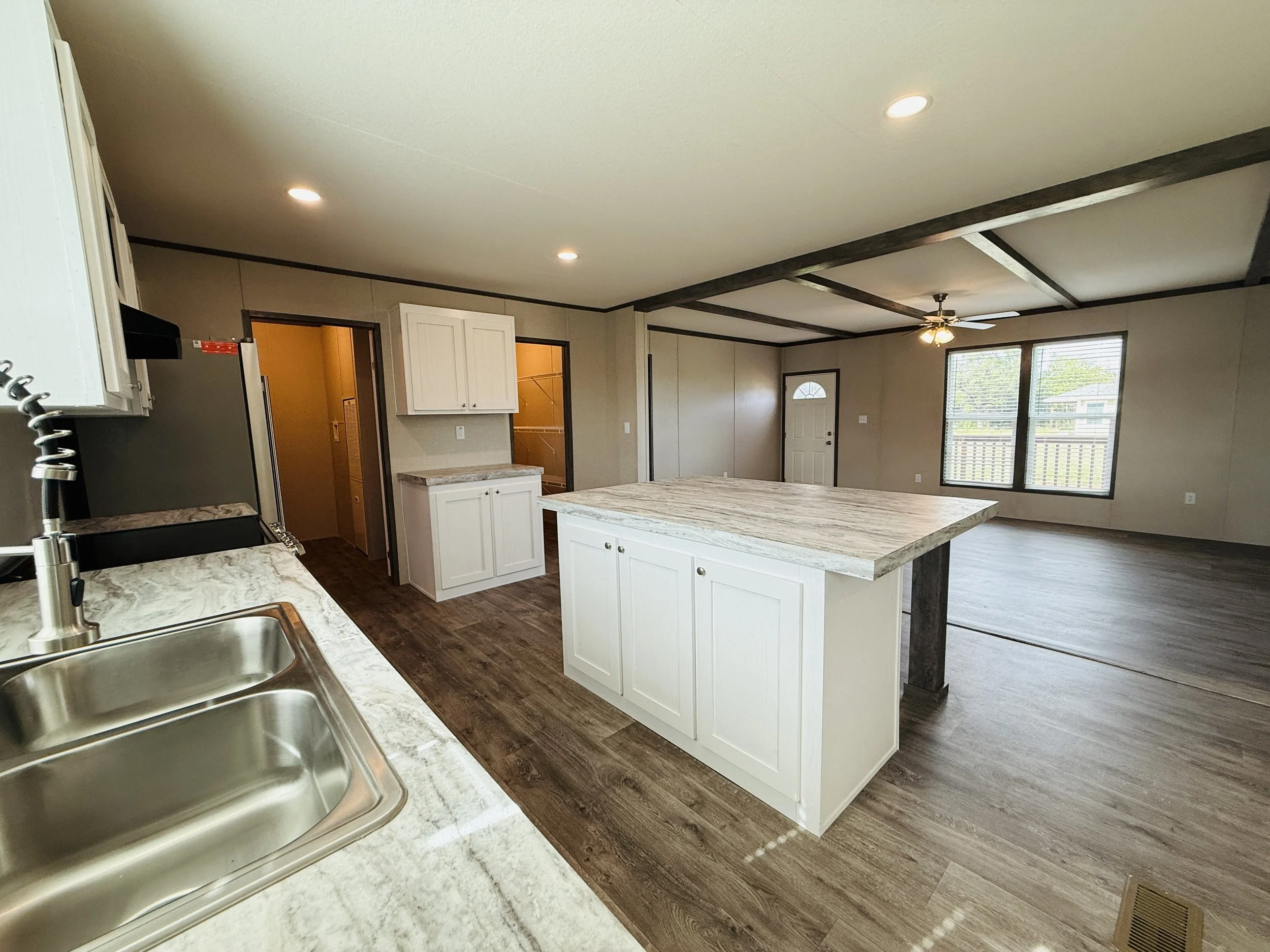 Open-concept kitchen and living area with white cabinets, a kitchen island, stainless steel sink, wood flooring, windows, and a ceiling fan.