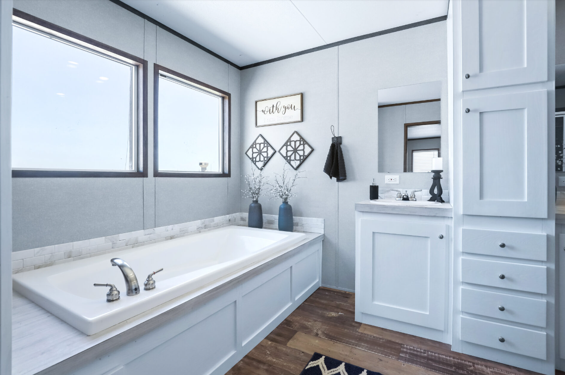 Bathroom with a white bathtub, two large windows, wall decor with a sign that says "with you," and a white vanity with a mirror reaching the ceiling, featuring a black lamp and black soap dispenser.