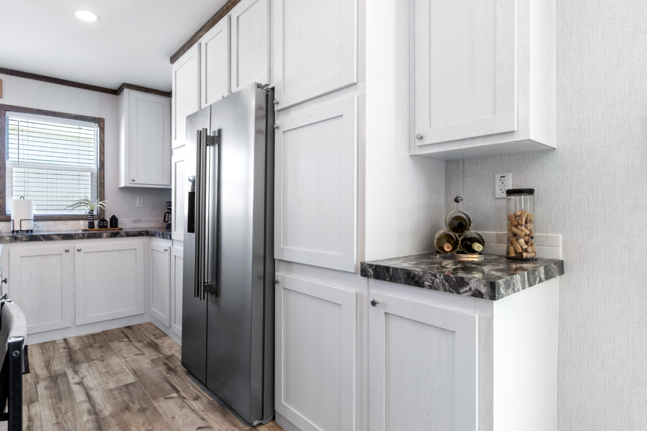 White kitchen with black granite countertops, stainless steel refrigerator, and decorated with wine bottles and a jar of corks.