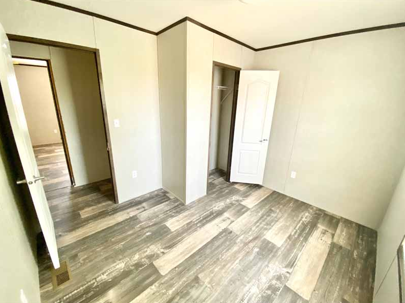 Empty bedroom with beige walls, wood-patterned flooring, open closet door, and doorway to another room.