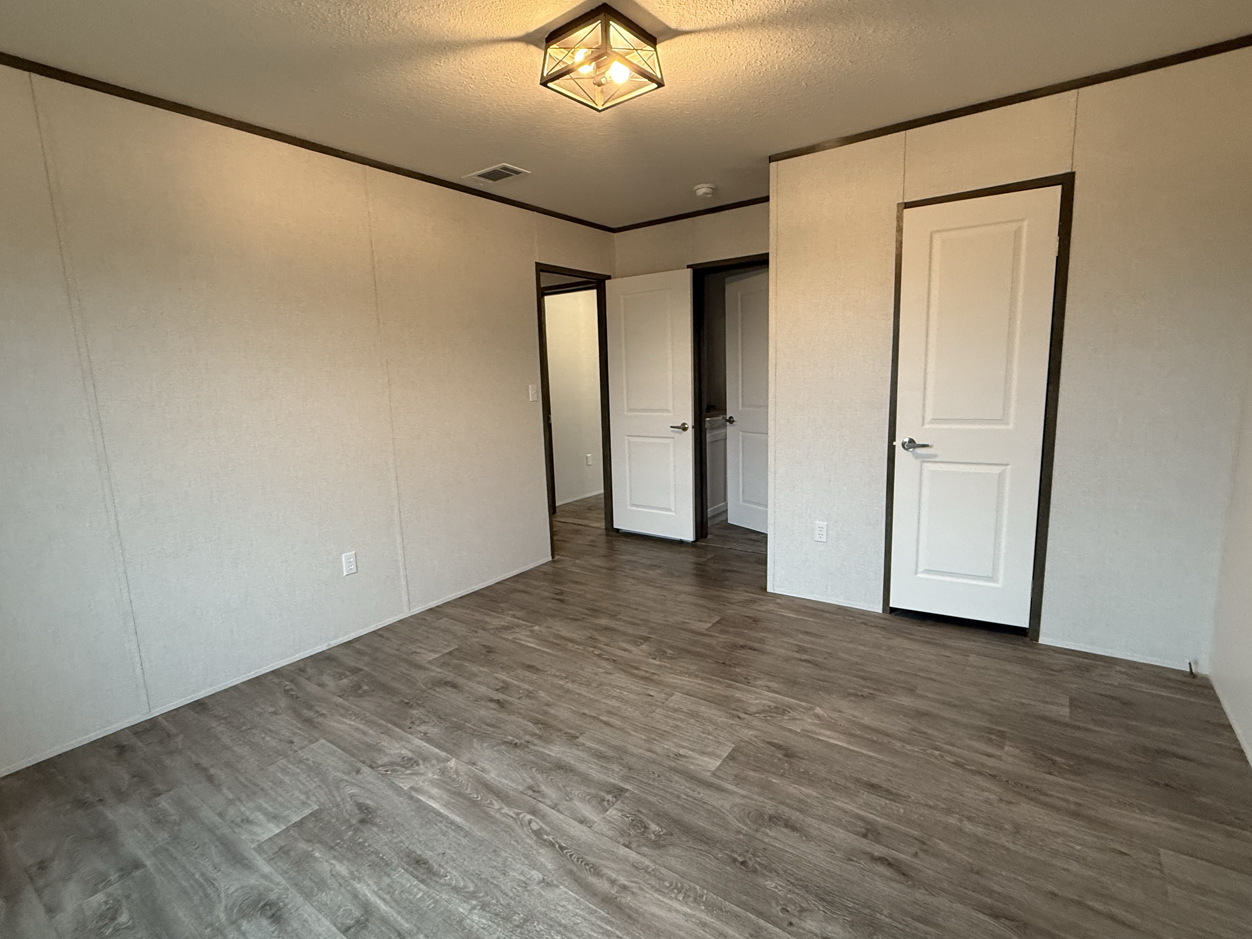 Empty room with beige walls, wood-look flooring, white doors, and ceiling light fixture.
