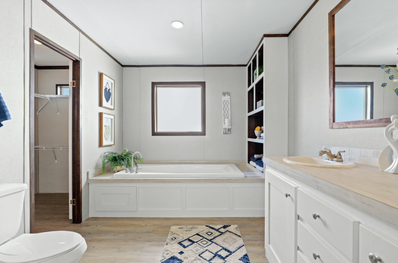 Bathroom with a bathtub, a vanity with a sink, a mirror, a window, open closet, and a toilet, with wooden flooring and white walls.