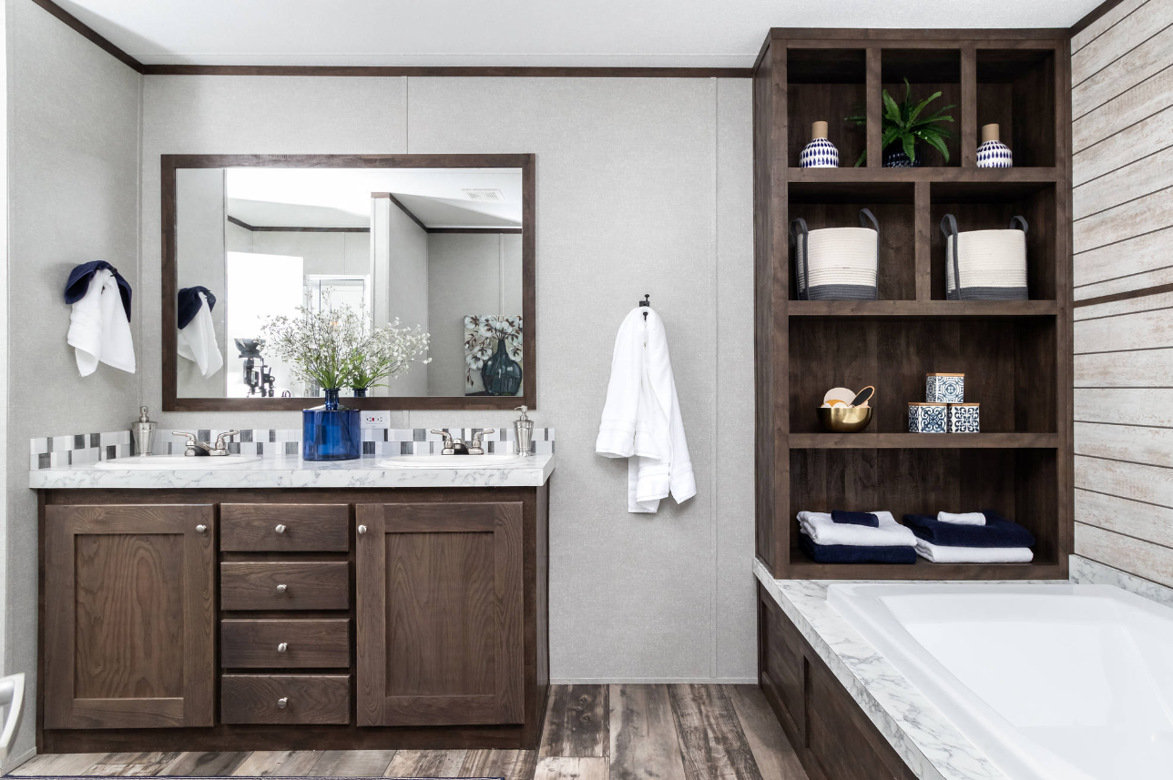 Bathroom with dual sinks, large mirror, wooden cabinetry, and shelves with decorative items and towels.