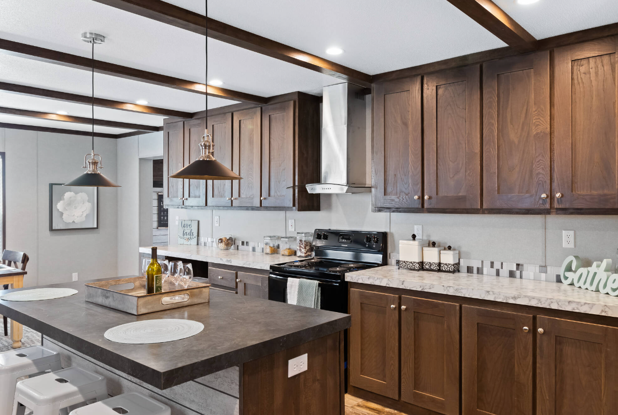 Modern kitchen with wooden cabinets, marble countertops, black stove, stainless steel vent hood, island with barstools, pendant lights, and decorative jars.