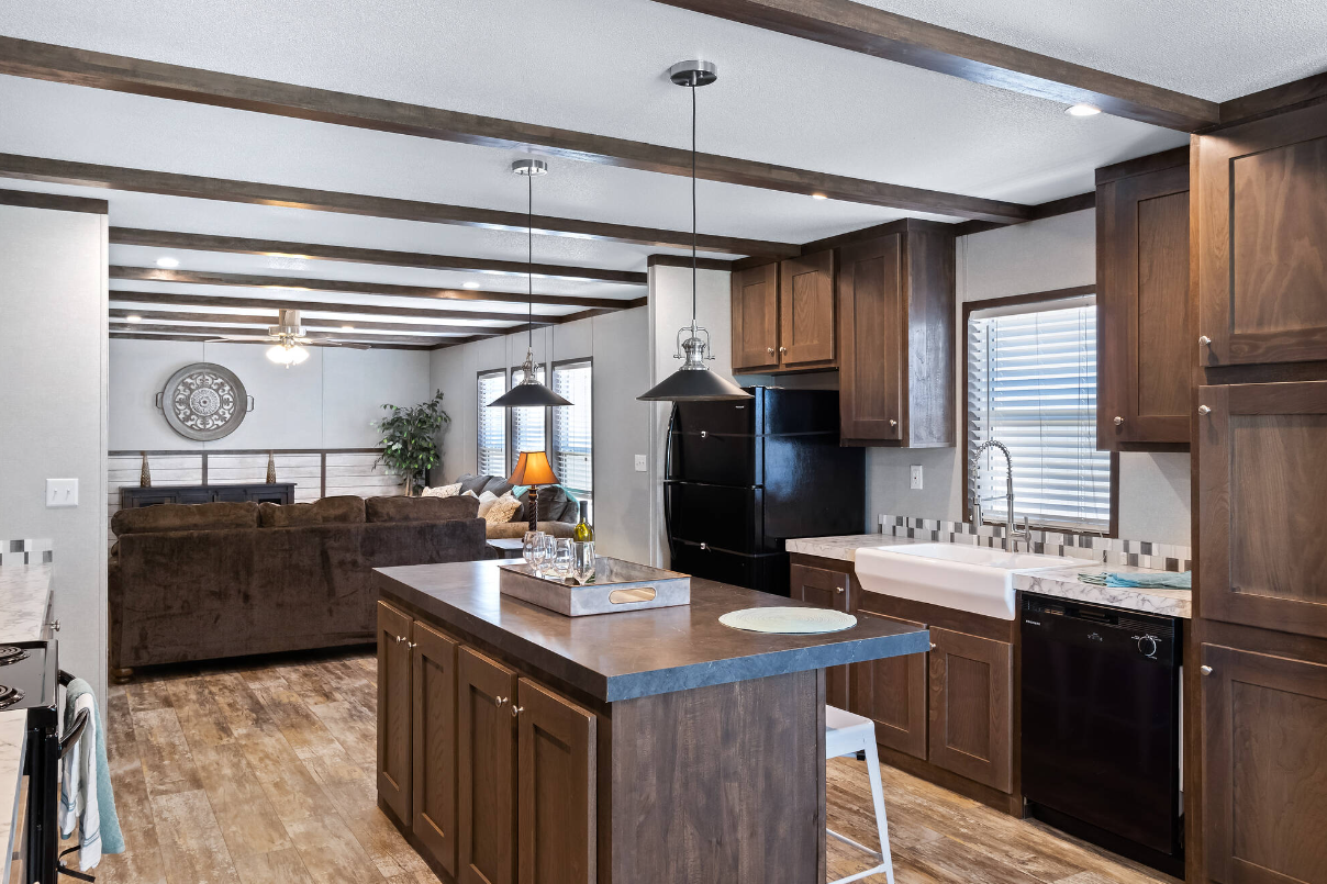 Open-concept kitchen and living room with wooden cabinets, black appliances, a central kitchen island, and a brown sofa in the living area.