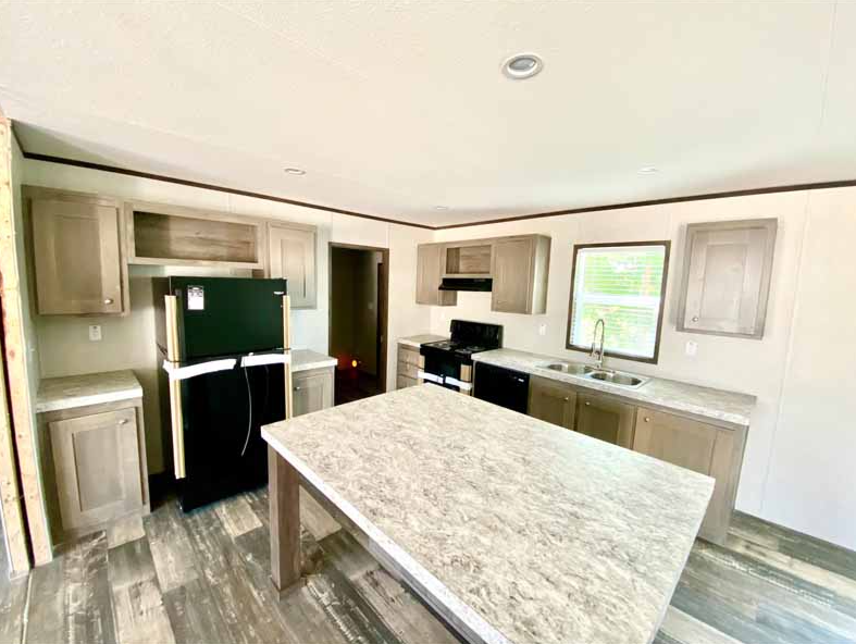Empty kitchen with light wood cabinets, a black refrigerator, oven, dishwasher, and a large island with a granite countertop, under a ceiling with recessed lighting, and a window with blinds.