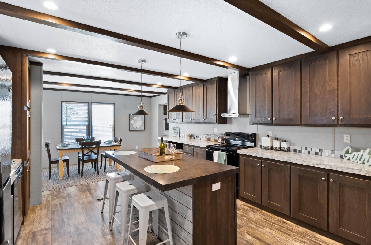 Modern kitchen with wooden cabinets, a kitchen island with bar stools, stainless steel appliances, and a dining area with a table and four chairs.
