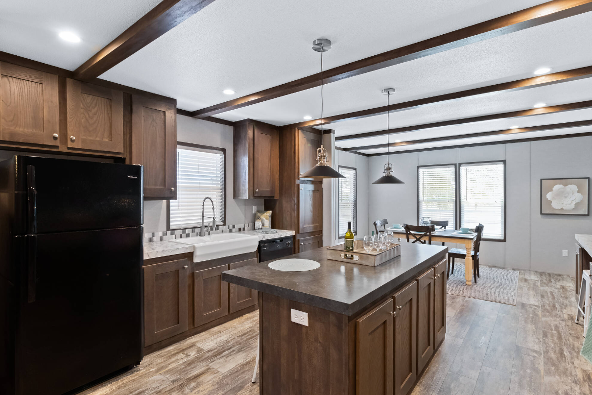 Kitchen with dark wood cabinets, black refrigerator, white farmhouse sink, and a kitchen island with a bottle of wine and glasses, in front of a dining area with a table and four chairs.