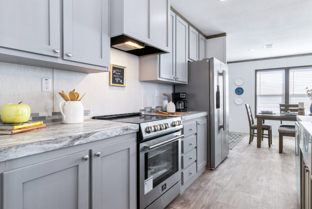 Modern kitchen with gray cabinets, marble countertop, stainless steel appliances, and a dining area with large windows.
