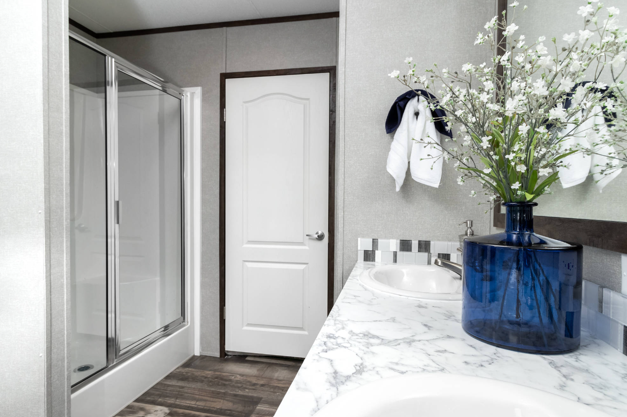 Bathroom with a white marble countertop, a blue vase with white flowers, a mirror, and a shower enclosure.