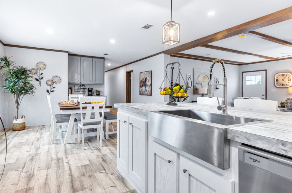 Modern kitchen with white cabinets, marble countertops, stainless steel sink, and a dining area featuring a white and wood table with chairs, decorated with artwork, plants, and a hanging light fixture.