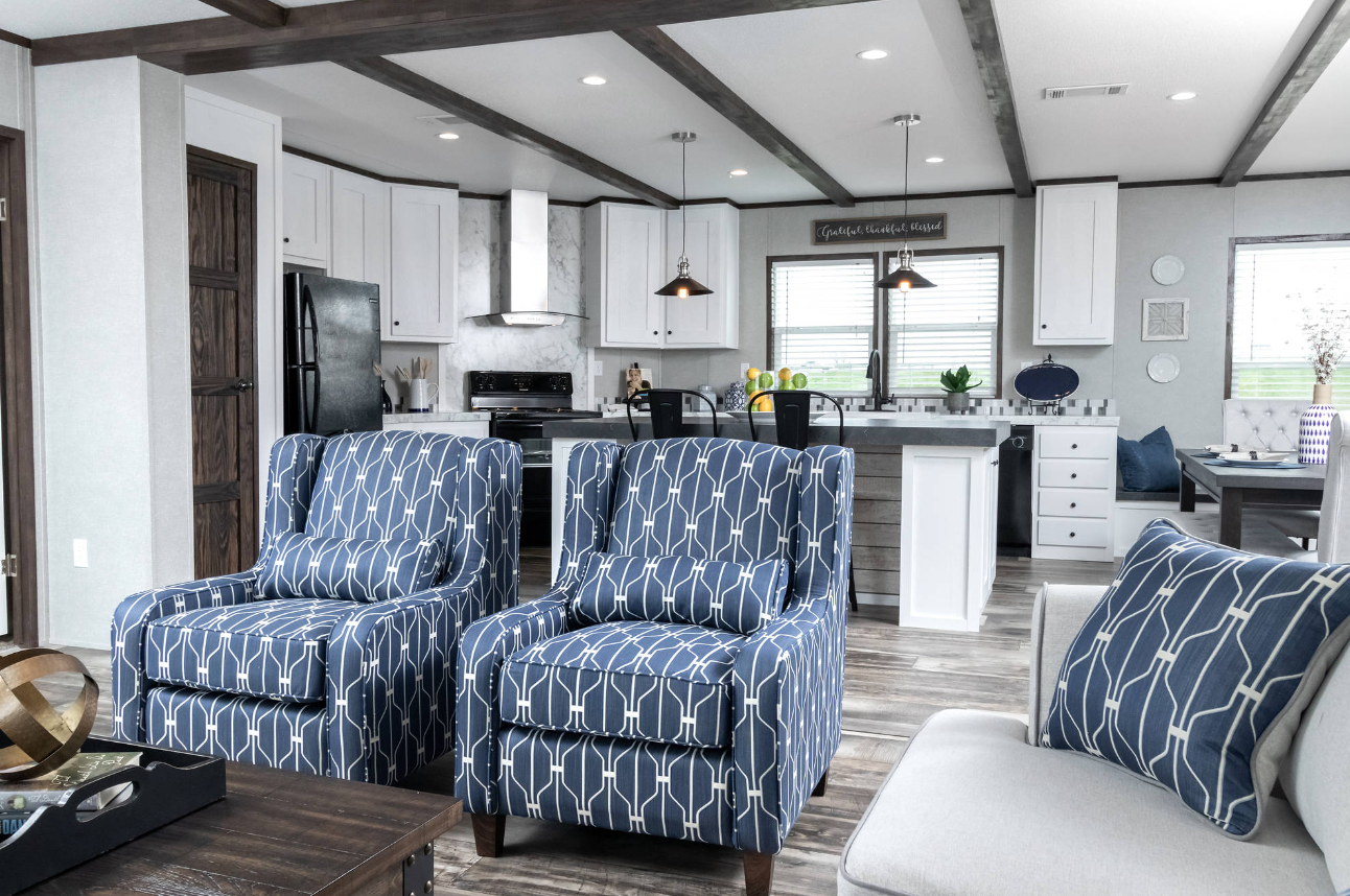 Open-concept living room and kitchen with blue patterned armchairs, white cabinets, black appliances, and wood accents.